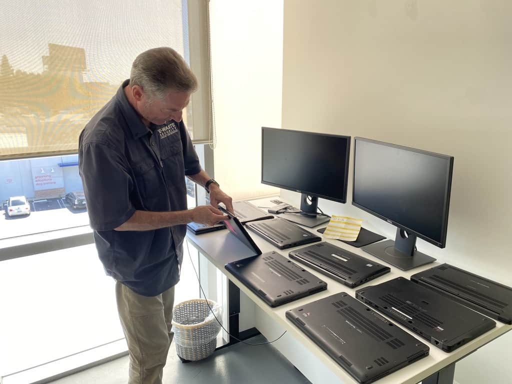 A man is standing in front of a table full of laptops.
